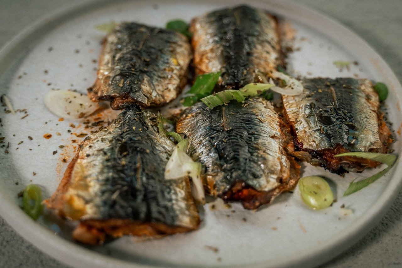 Gegrilde sardines met gesneden groene uien op een witte schaal.