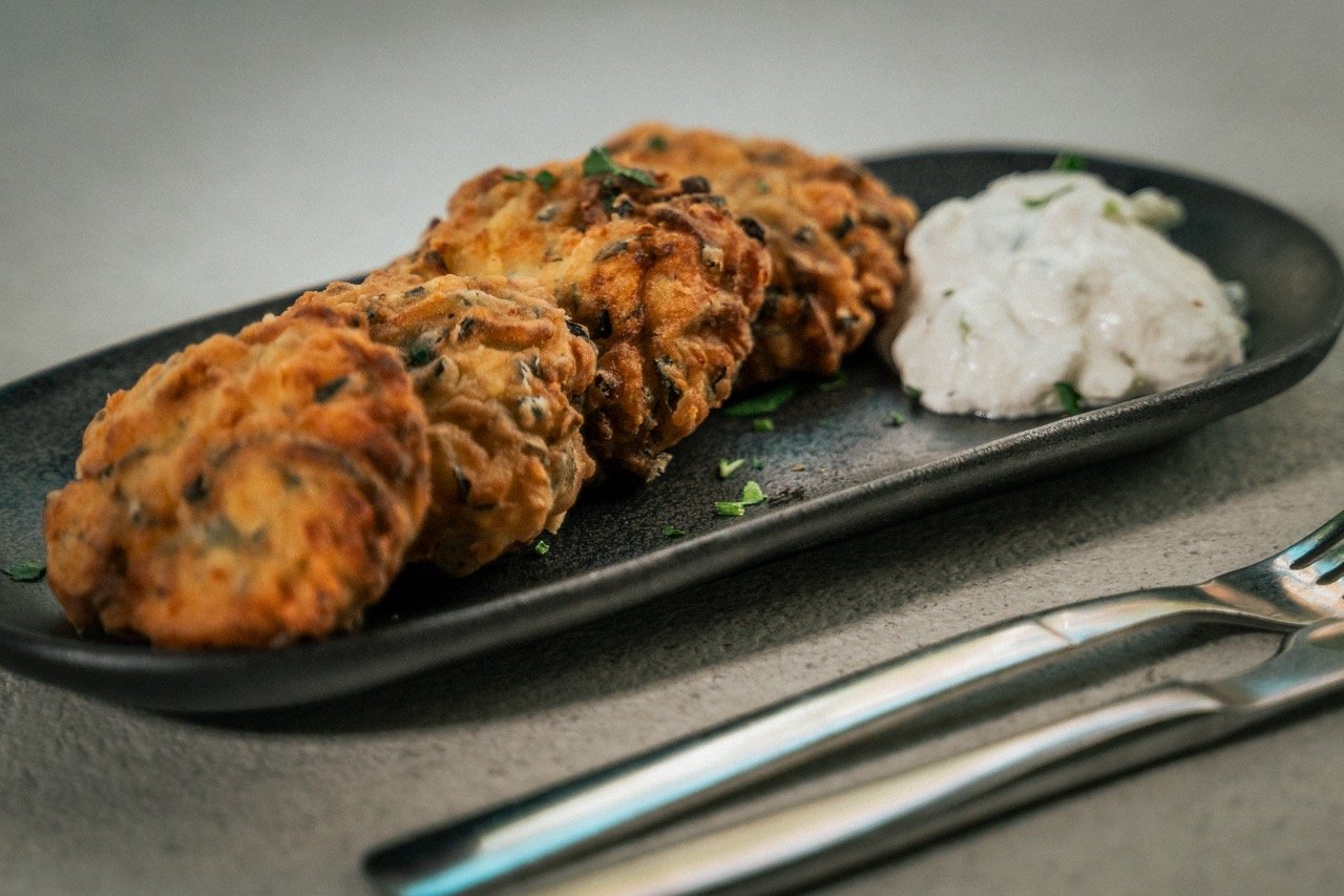 Gekookte kroketten met een witte saus op een zwarte schaal, met een vork en mes ernaast.